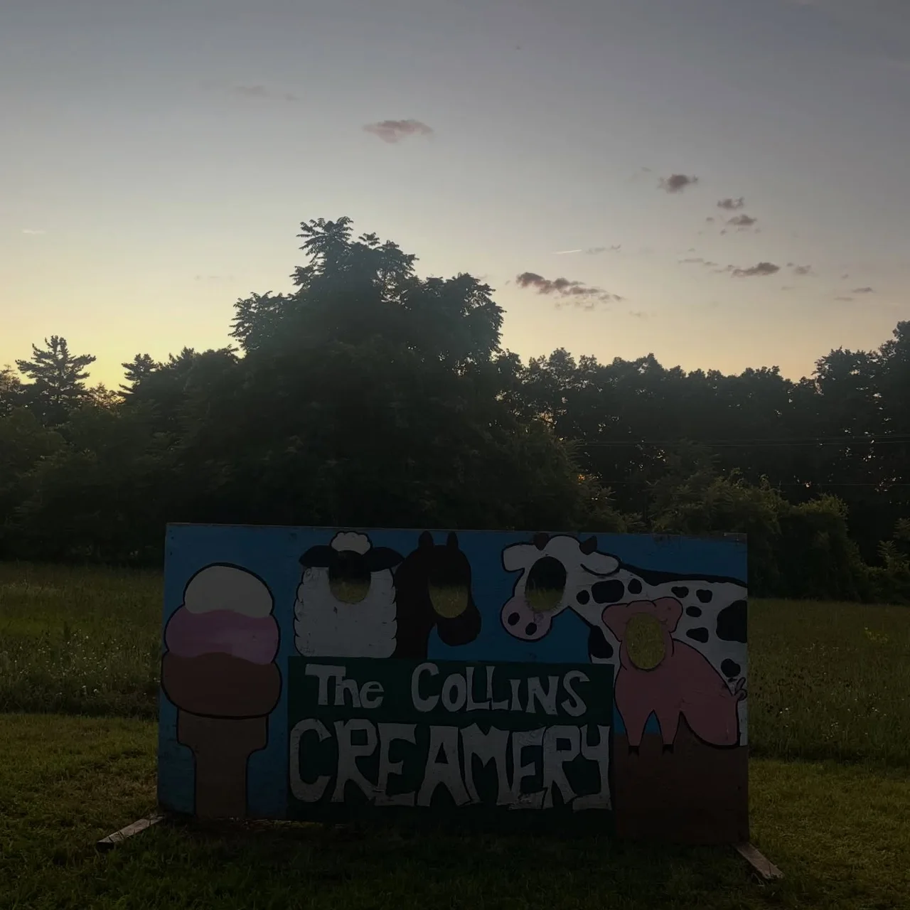 The painted face cutout sign with the cow, sheep, and ice cream cone at dusk