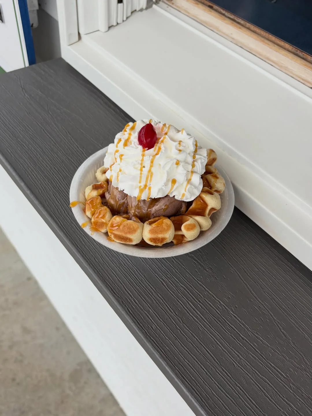 A waffle sundae with caramel drizzle, whipped cream, and a cherry